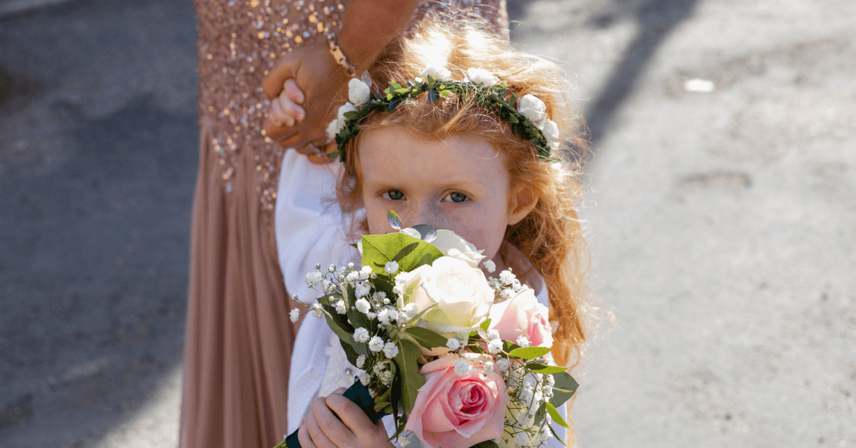 A little girl wearing a floral crown holding a bouquet in front of her face.