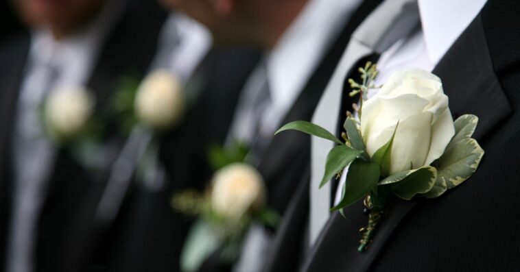 Unidentifiable groomsmen in black wearing white rose boutonnieres.