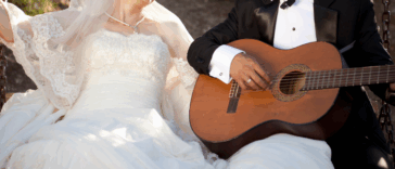 A groom sitting next to a bride, playing the guitar.