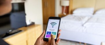 Over the shoulder view of a businesswoman connecting to the mobile wifi in a hotel room. Wifi icon on mobile phone display.