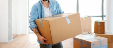 Closeup front view of a smiling young man carrying boxes as he moves into his new apartment.