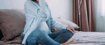 A pregnant woman sitting on a bed, resting her head in her hands.