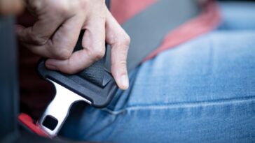 Close up of a woman's hand pulling a seat belt in her car.