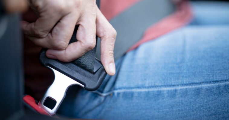 Close up of a woman's hand pulling a seat belt in her car.