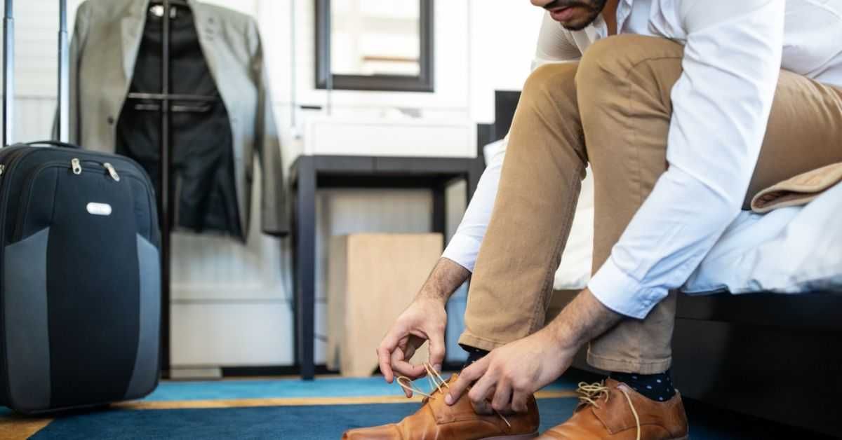 Cropped shot of man removing his shoe while sitting on hotel bed.