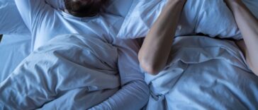 A stressed woman, covers her face with a pillow, she cannot fall asleep because her husband is snoring in bed at night.