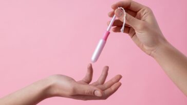 A close up on a pink background with two hands of women passing a tampon in applicator.