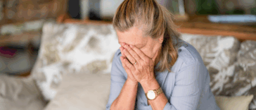 A woman sitting on the. sofa with her head in her hands.