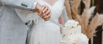 Close-up of a bride and groom's hands cutting into their wedding cake.