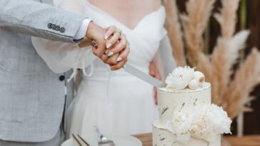 Close-up of a bride and groom's hands cutting into their wedding cake.
