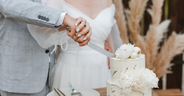 Close-up of a bride and groom's hands cutting into their wedding cake.