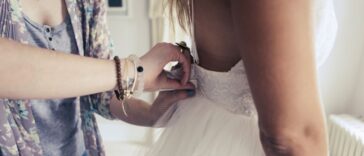Midsection shot of a bride to be standing in an elegant wedding dress and looking at herself in the mirror during a fitting in a bridal shop, with the stylist making small adjustments to the dress.