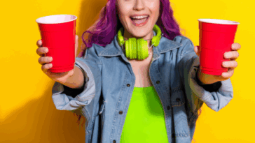 A woman with purple hair holding two red plastic cups.