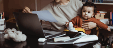 A woman. at her desk with a baby on her lap.