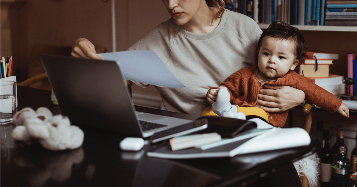 A woman. at her desk with a baby on her lap.