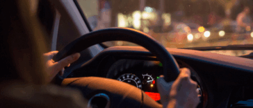 A woman behind the wheel of a car with the. gas gague on empty.