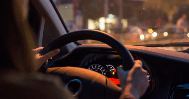 A woman behind the wheel of a car with the. gas gague on empty.