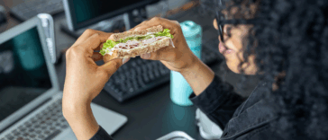 A woman eating a sandwich while sitting at her computer.
