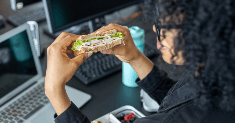 A woman eating a sandwich while sitting at her computer.