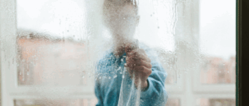A person claning windows with their face hidden by the spray.