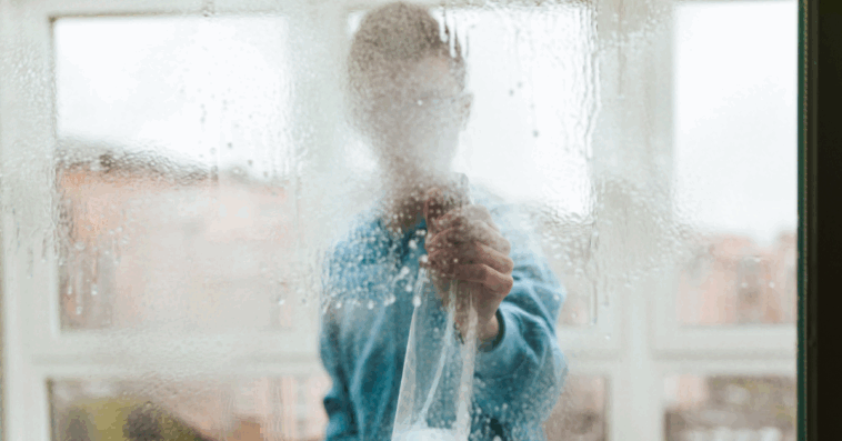 A person claning windows with their face hidden by the spray.