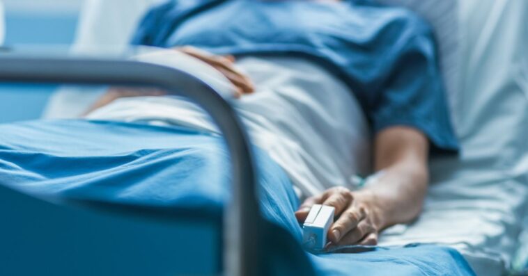 In the Hospital Sick Male Patient Sleeps on the Bed. Heart Rate Monitor Equipment is on His Finger.