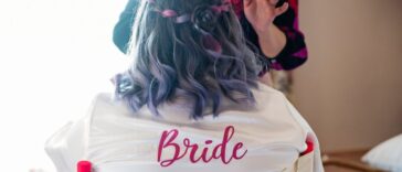 A bride gets her make-up done. She is not facing the camera, the back of her robe reads bride in red letters.