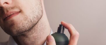 Handsome unshaven man applying perfume on neck, closeup. Space for text.