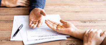 Two people holding wedding rings resting their hands on divorce papers.