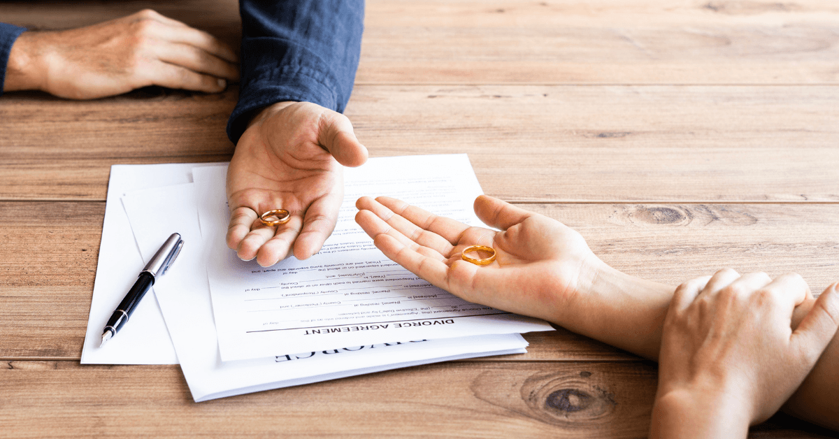 Two people holding wedding rings resting their hands on divorce papers.