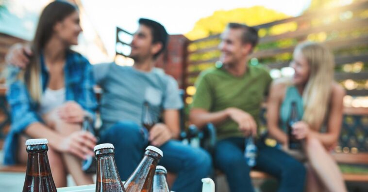 Shot of bottled beers chilling in a cooler box with a group of friends hanging out in the background.