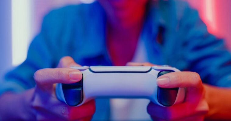 Close up of a young woman playing a video game console in neon lighted living room at home.