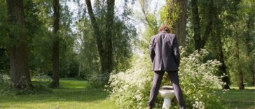 Businessman using a bush as a toilet in a park.