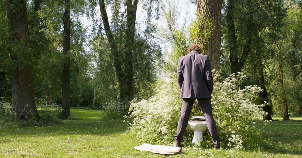Businessman using a bush as a toilet in a park.