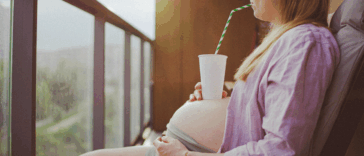 A pregnant woman drinking from a cup resting on her baby bump.