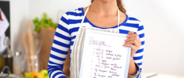 Woman in the kitchen at home, standing near stove while holding a recipe.