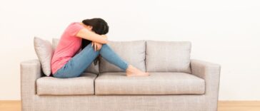 Young, beautiful woman sadly sitting on the sofa with her head in her lap.