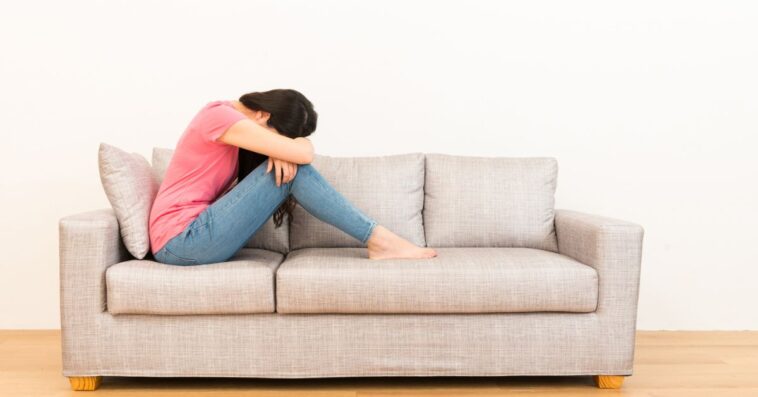 Young, beautiful woman sadly sitting on the sofa with her head in her lap.