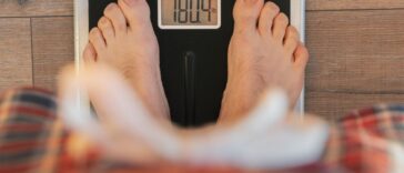 View from Above: Man Weighing In on Scale on Wooden Floor at Home.