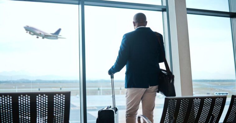 Airport, suitcase and businessman waiting to board flight by the terminal for corporate work trip. Travel, luggage and professional male traveler watching flying plane by a window in terminus lounge.