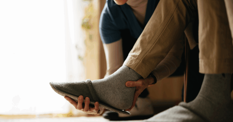 A woman helping a man take off his slippers.