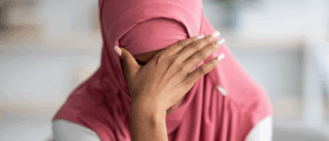 A woman wearing a hijab with her head in her hands.