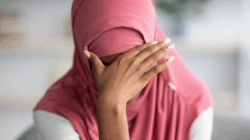 A woman wearing a hijab with her head in her hands.