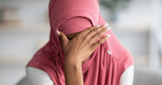 A woman wearing a hijab with her head in her hands.