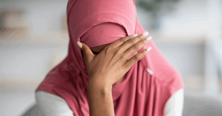 A woman wearing a hijab with her head in her hands.
