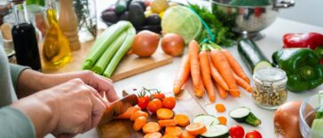 Close up of a woman's hands slicing fresh organic carrots on kitchen counter.