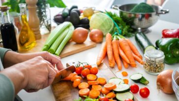 Close up of a woman's hands slicing fresh organic carrots on kitchen counter.