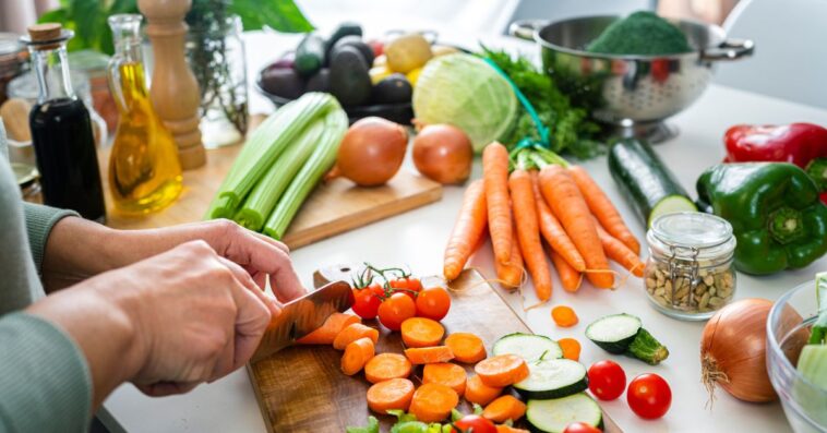 Close up of a woman's hands slicing fresh organic carrots on kitchen counter.