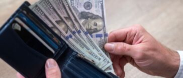 Hands holding a wallet with a small amount of US dollars, close up.
