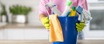 A woman standing behind a bucket of cleaning supplies.